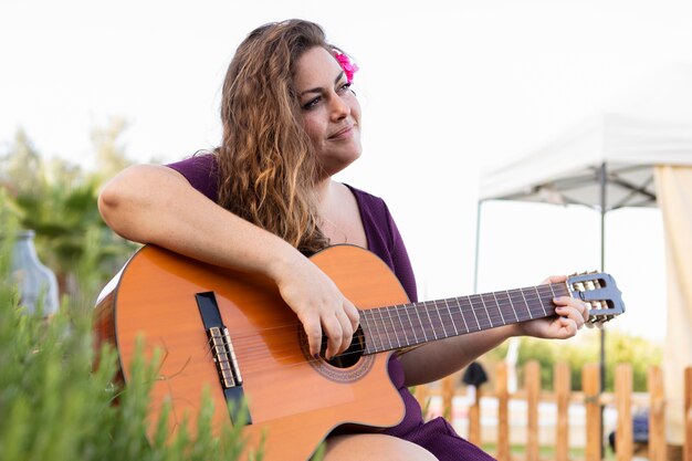 Vue côté, de, femme, à, fleur, dans, cheveux, jouer guitare