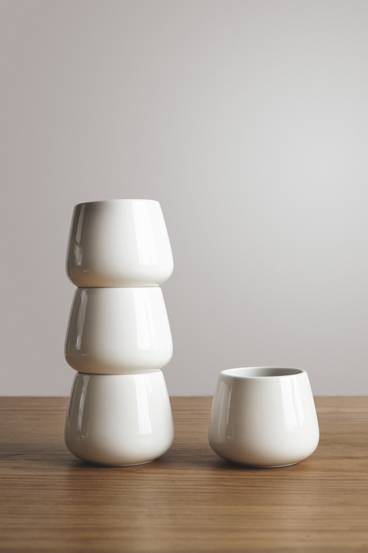 Photo gratuit vue de côté haut de forme étroite blanc tasses à café simples en pyramide sur une table en bois épaisse isolée