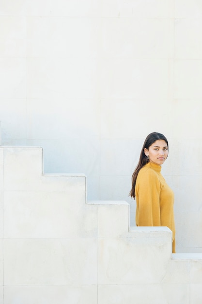 vue de côté d&#39;une jeune femme regardant la caméra debout près d&#39;un escalier