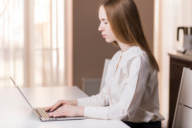 Vue de côté de la jeune fille à étudier avec son ordinateur portable