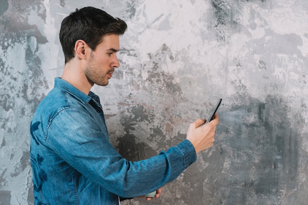 Vue côté, de, jeune homme, debout, devant, mur grunge, à, téléphone portable