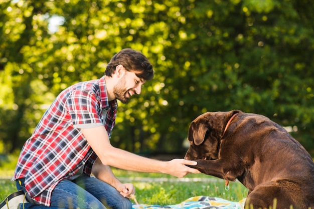 Photo gratuite vue de côté d'un jeune homme souriant, jouant avec son chien dans le parc