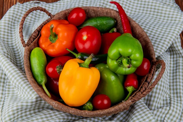 Vue de côté de légumes frais poivrons colorés piments rouges tomates et concombres dans un panier en osier sur tissu à carreaux