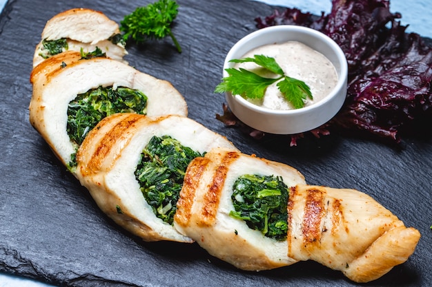 Photo gratuite vue de côté poitrine de poulet farcie aux épinards et sauce sur la table