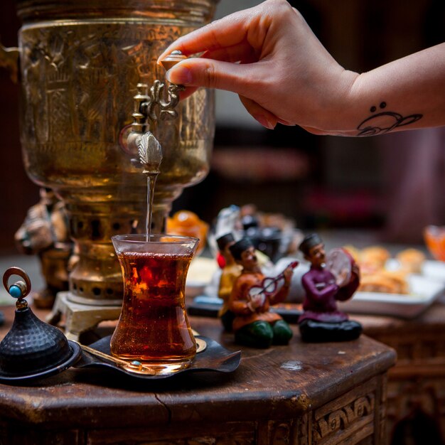 Vue de côté samovar avec verre de thé et figurines et main humaine dans le tableau sur le restaurant