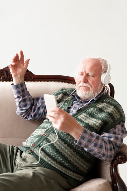 Vue de côté senior sur un canapé en jouant de la musique