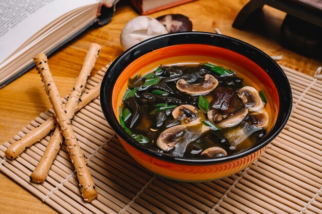 Vue de côté soupe aux champignons avec oignon de printemps et bâton de pain sur la table