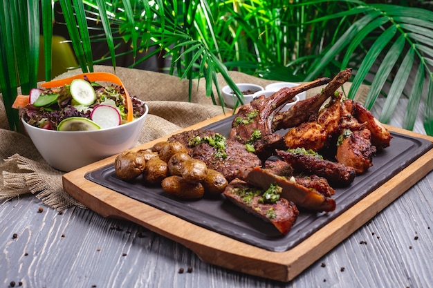 Vue de côté steak avec côtes levées avec poulet frit et pommes de terre sur la planche et avec salade de légumes