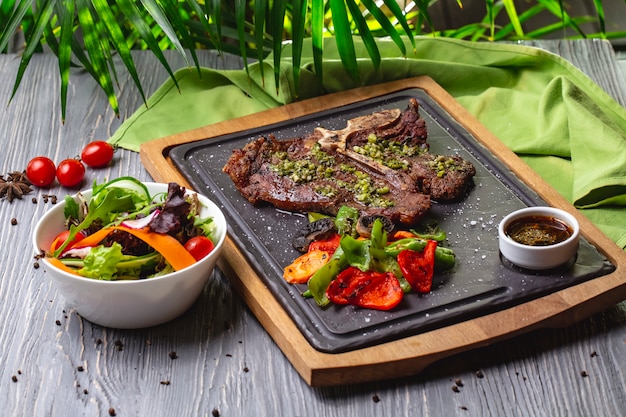 Vue de côté steak d'os avec légumes grillés et sauce sur la planche avec salade de légumes