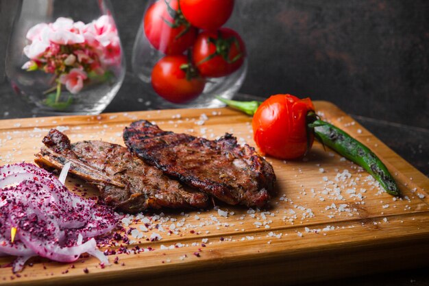Vue de côté steak avec tomate et oignon en planche à steak