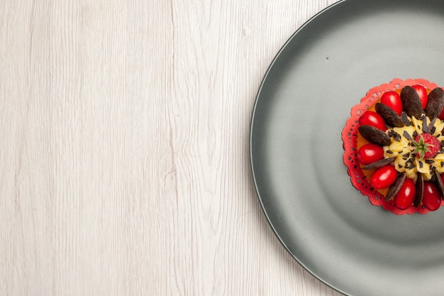 Photo gratuite vue de côté supérieur droit gâteau au chocolat arrondi avec cornouiller et framboise au centre sur la table en bois blanc