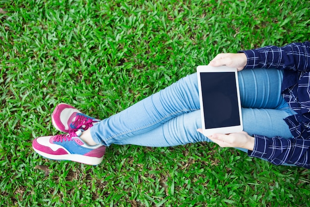 Vue croisée de la fille utilisant la tablette sur l&#39;herbe