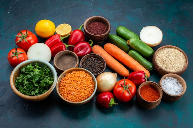 Photo gratuite vue demi-dessus des légumes frais avec des légumes verts et des assaisonnements sur un bureau bleu foncé.