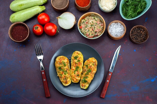 Vue demi-dessus des légumes frais avec de la viande hachée verte, des courges cuites et des assaisonnements sur le bureau violet foncé.