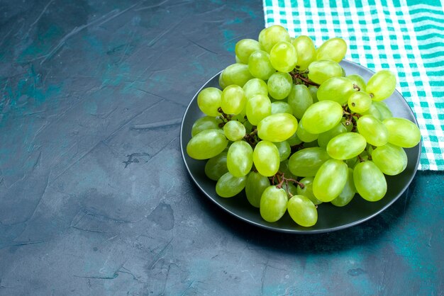 Vue demi-dessus des raisins verts frais fruits juteux moelleux à l'intérieur de la plaque sur le bureau bleu foncé.