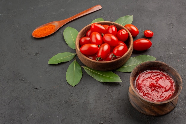 Vue de dessous un bol de tomates cerises laurier laisse une cuillère en bois et un bol de ketchup sur la table noire