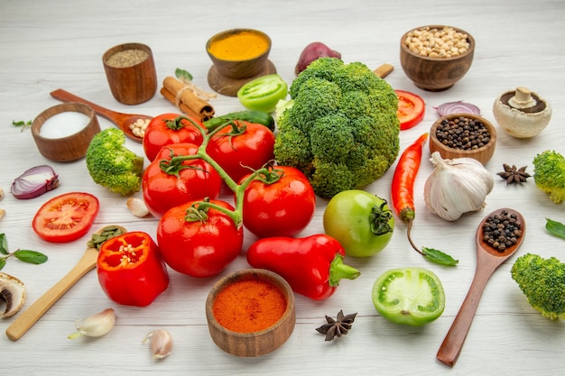 Vue de dessous bols de branche de tomate avec différents haricots et épices cuillères en bois de brocoli ail sur table grise