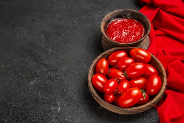 Vue de dessous des bols avec des tomates cerises et une serviette rouge ketchup sur fond sombre