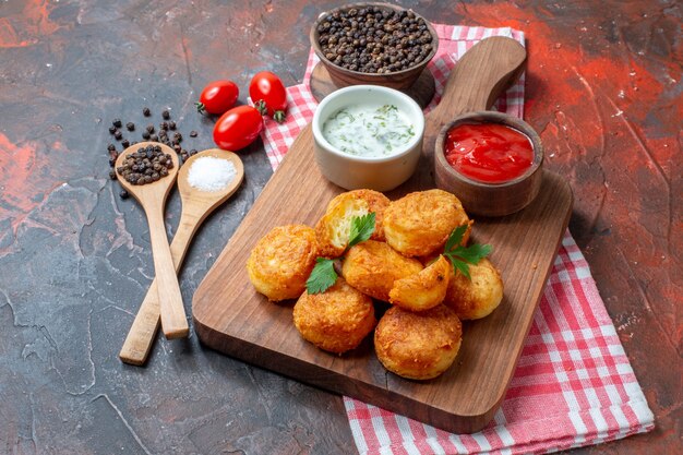 Vue de dessous boules de fromage sauces dans des bols sur planche de bois tomates cerises cuillères en bois poivrons noirs sur fond sombre