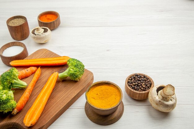 Vue de dessous carottes et brocolis hachés sur planche à découper champignons différentes épices dans des bols sur table place libre