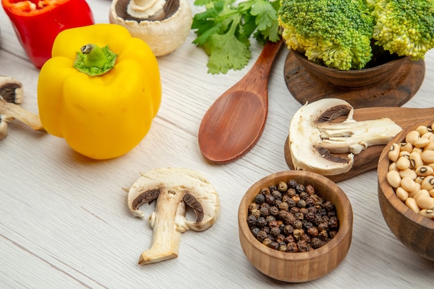 Photo gratuite vue de dessous carottes sur planche à découper champignons différentes épices dans des bols poivrons cuillères en bois sur table