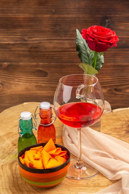 Vue de dessous des copeaux de verre à vin ballon dans un bol bouteilles rouges et vertes rose rouge sur surface brune