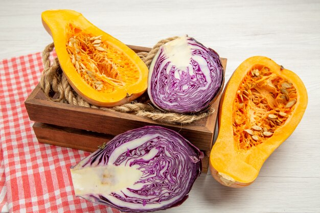 Vue de dessous courge musquée et chou rouge coupés en corde à double dans une boîte en bois nappe à carreaux rouge et blanc sur table grise