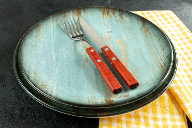 Vue de dessous le couteau et une fourchette sur une assiette sur une serviette à carreaux jaune et blanc sur fond noir