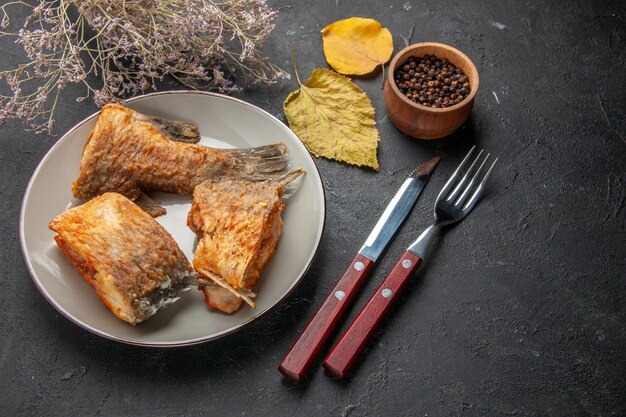 Vue de dessous de délicieux alevins de poisson sur une fourchette et un couteau branche de fleurs séchées poivre noir dans un bol en bois sur un tableau noir