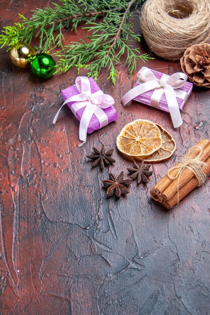 Vue de dessous détails de noël branches de pin boules d'arbre de noël fil de paille cannelle anis étoilé tranches de citron séchées cadeaux de noël sur fond rouge foncé espace libre