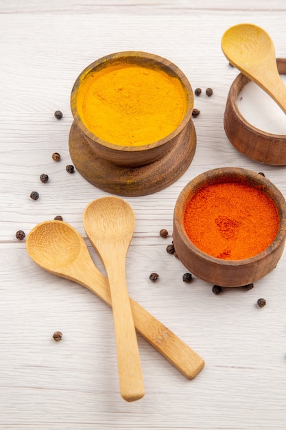 Photo gratuite vue de dessous diverses épices curcuma poivre rouge en poudre sel dans un petit bol cuillères en bois éparpillés poivre noir sur table grise