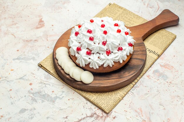 Vue de dessous gâteau avec crème pâtissière blanche et chocolat blanc sur planche à découper sur papier journal sur table gris clair