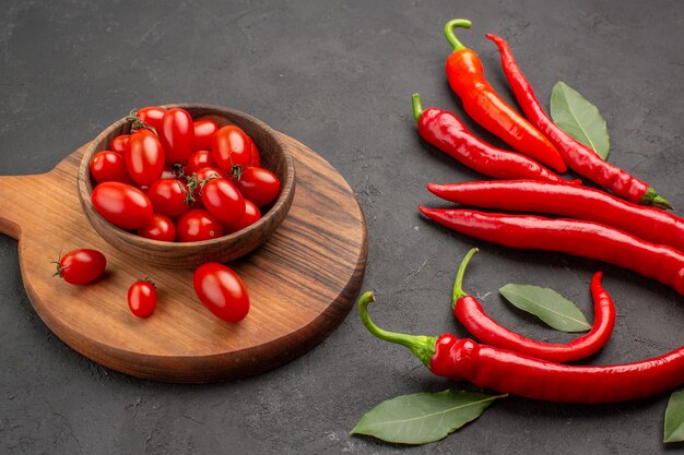 Vue de dessous gros plan poivrons rouges et payer les feuilles et un bol de tomates cerises sur la planche à découper ovale sur tableau noir