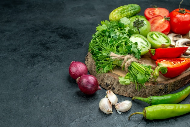 Vue de dessous légumes champignons tomates rouges et vertes poivrons verts sur planche rustique oignons rouges piments ail sur table noire espace libre