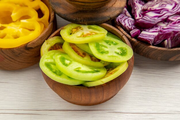 Vue de dessous légumes coupés chou rouge coupé poivrons jaunes coupés tomates vertes dans des bols sur tableau blanc