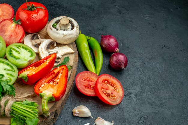 Vue de dessous légumes frais champignons tomates rouges et vertes poivrons verts sur planche rustique piments ail oignons sur table sombre place libre