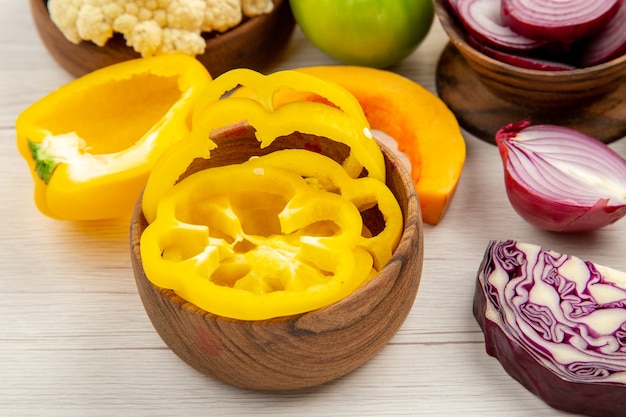 Vue de dessous légumes frais poivrons jaunes choux rouges chou-fleur citrouilles oignons coupés dans des bols sur une table en bois blanc