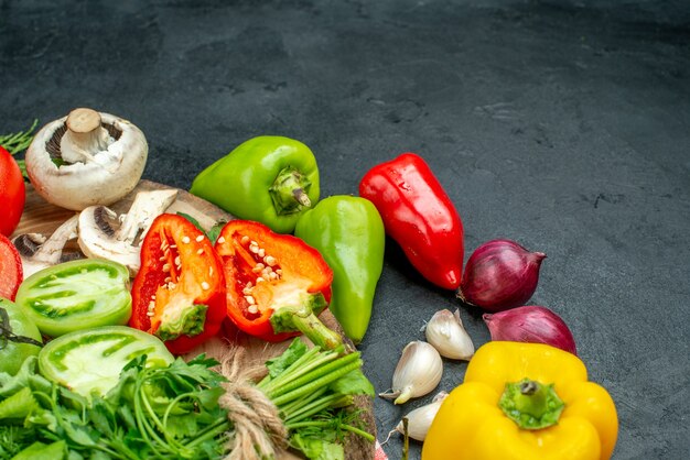 Vue de dessous légumes tomates poivrons rouges champignons verts sur planche rustique piments oignon rouge ail sur table noire espace libre