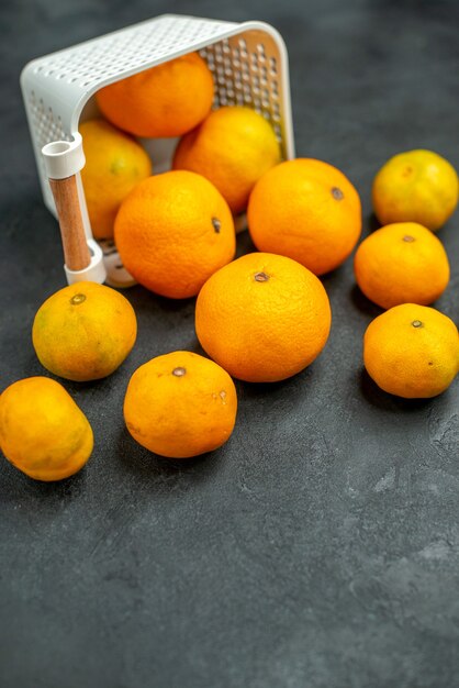 Vue de dessous des mandarines et des oranges éparpillées du panier en plastique sur un espace libre sombre