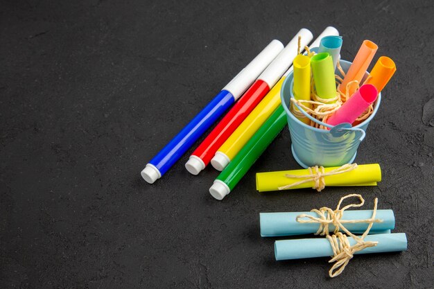 Vue de dessous des marqueurs de couleur enroulés des notes autocollantes attachées avec une corde dans un petit seau sur un espace libre de table noire