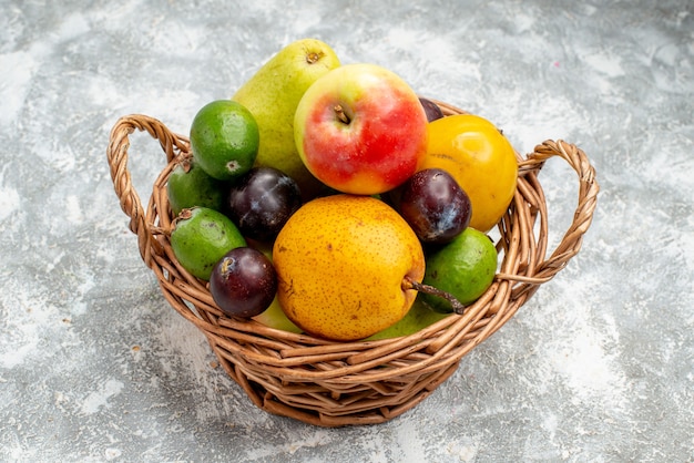 Photo gratuite vue de dessous panier en osier en plastique avec pommes poires feykhoas prunes et kaki sur la table grise avec copie espace