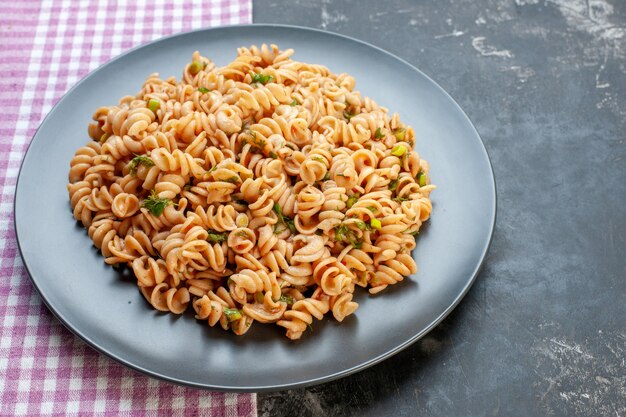 Vue de dessous des pâtes rotini sur une assiette ronde sur une nappe à carreaux blanc rose sur une table grise