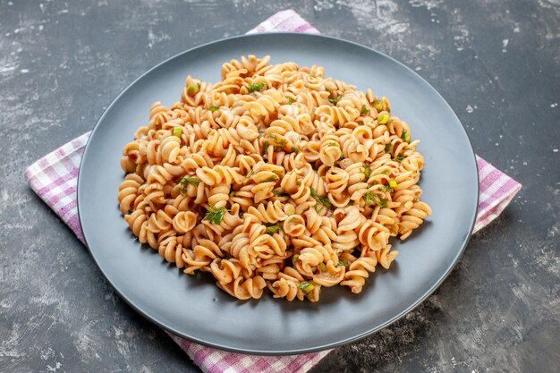 Vue de dessous des pâtes rotini sur une assiette ronde sur une serviette à carreaux rose blanc sur une table grise