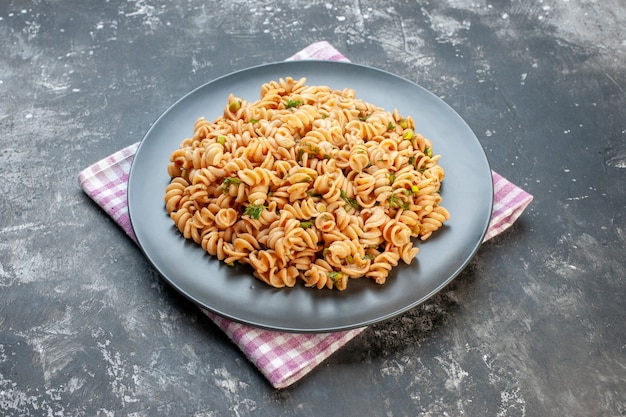 Vue de dessous des pâtes rotini sur une assiette ronde sur un torchon à carreaux blanc rose sur une table grise