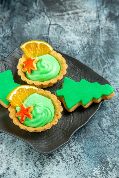 Vue de dessous de petites tartes avec des biscuits de Noël à la crème pâtissière verte sur une plaque noire sur une surface grise