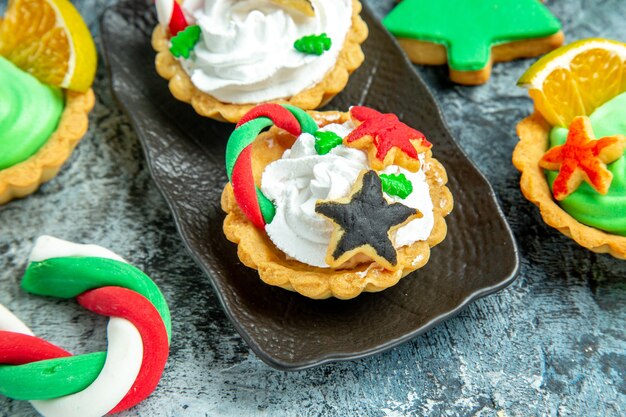 Vue de dessous petites tartes de Noël sur plaque noire bonbons de Noël et biscuit sur table grise