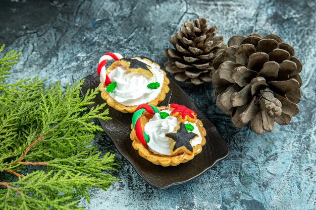 Vue de dessous petites tartes de Noël sur plaque noire pommes de pin branches de pin sur table grise