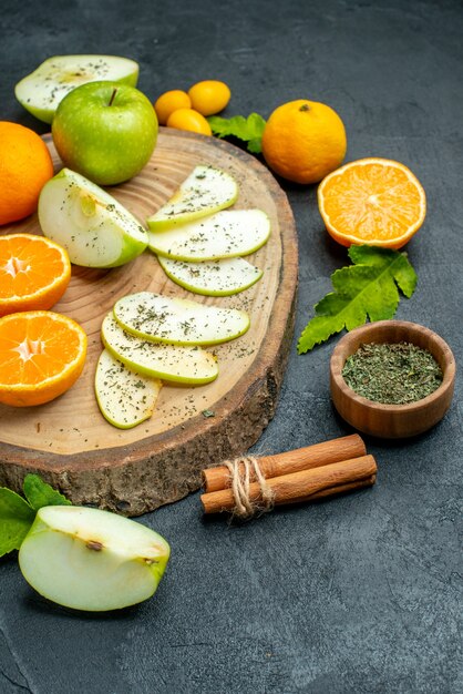 Vue de dessous des pommes et des mandarines coupées sur des cannelles rondes rustiques attachées avec de la poudre de menthe séchée à la corde dans un petit bol sur une table sombre