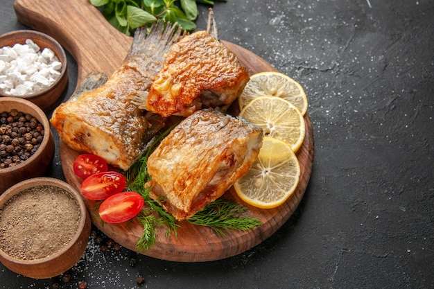 Vue de dessous de savoureux poissons frits tranches de citron coupés tomates cerises sur planche à découper sur fond noir