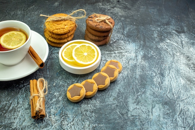 Vue de dessous tasse de thé aromatisée de biscuits au citron avec des biscuits au chocolat attachés avec des bâtons de cannelle de corde des tranches de citron sur une table grise place libre